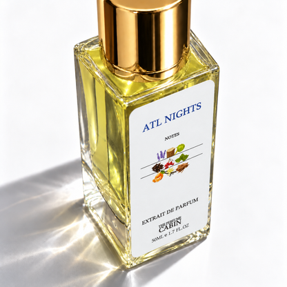 A square glass bottle of ATL NIGHTS Notes Extrait de Parfum by CABIN CLOSET, filled with pale yellow liquid and topped with a shiny gold cap, set against a bright white background with dramatic sunlit shadows.